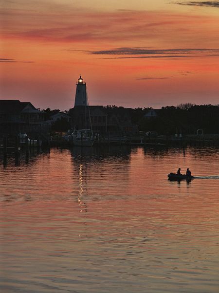 SunsetLighthousePICT1291-w.jpg - #0265_Sunset at Ocracoke Harbor:  Image captured Fall of 2005 while watching the sunset from our room balcony with a glass of wine on Ocracoke Island, North Carolina.  The boatmen going to shore from their sailboat and harbor lighthouse light were fortuitous in capturing the feeling of the moment.